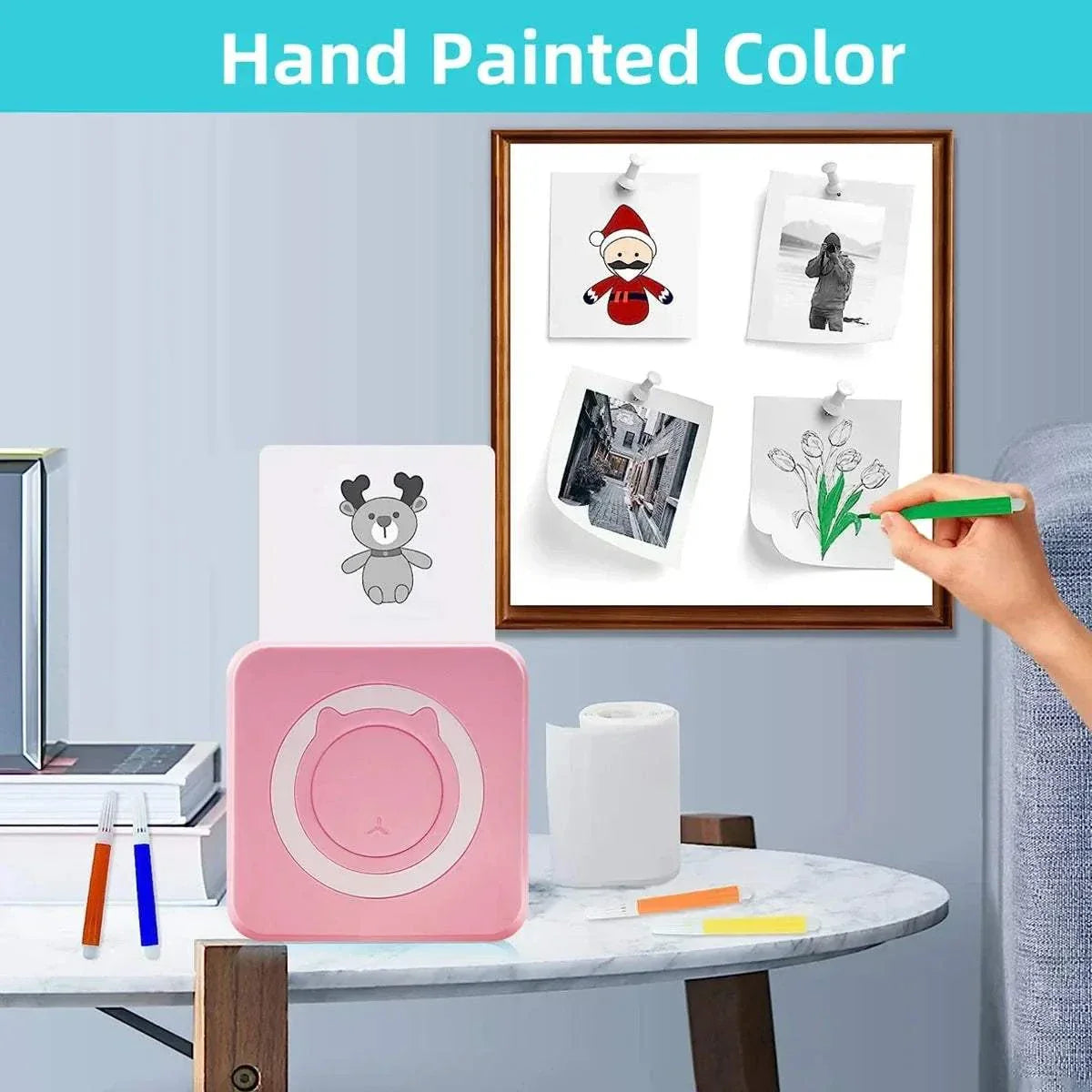 Portable mini thermal printer in pink, printing black-and-white hand-drawn photos, with a set of coloring tools on a white table.