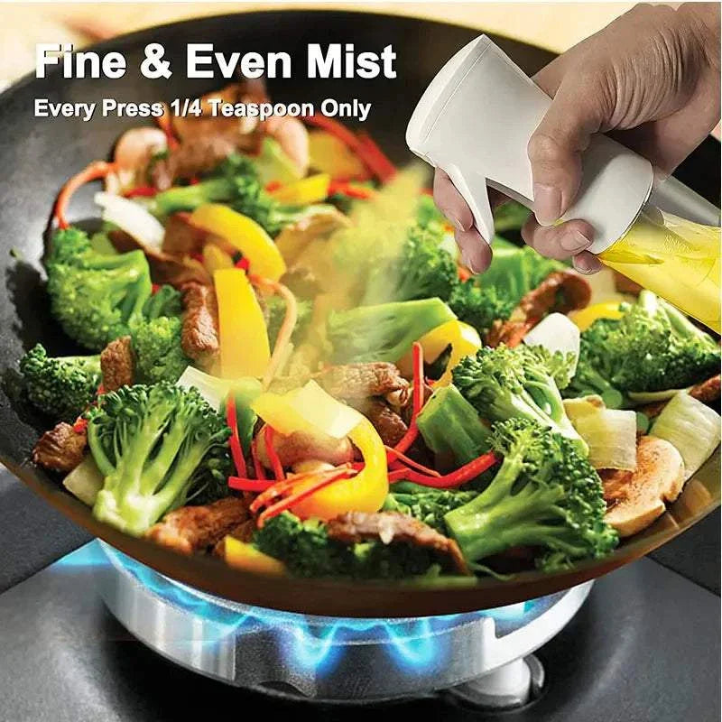 Oil spray bottle dispersing fine mist over vegetables in a frying pan.
